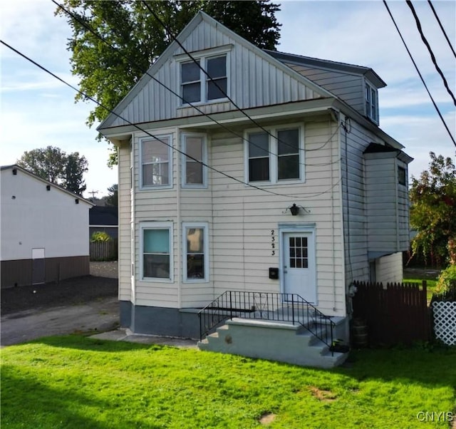 back of house with a yard, board and batten siding, driveway, and fence