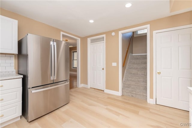 kitchen with white cabinets, light countertops, freestanding refrigerator, and light wood-style floors