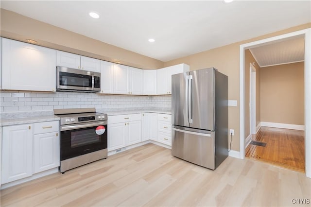 kitchen featuring light wood-style flooring, white cabinets, tasteful backsplash, and appliances with stainless steel finishes