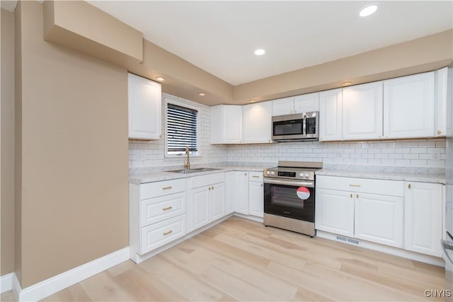 kitchen with baseboards, light wood-style flooring, a sink, appliances with stainless steel finishes, and white cabinetry