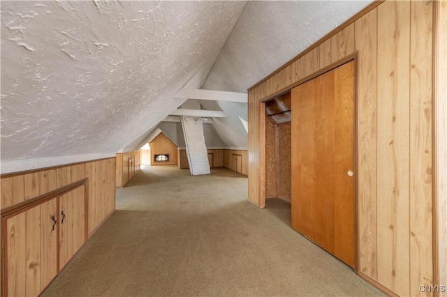 additional living space featuring lofted ceiling, light colored carpet, wood walls, and a textured ceiling