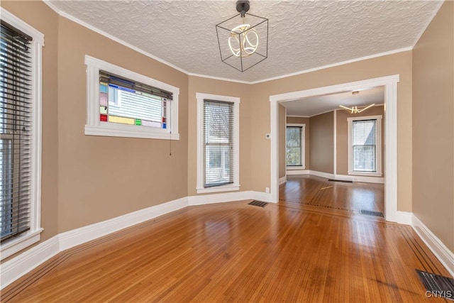 unfurnished room featuring visible vents, a notable chandelier, ornamental molding, wood finished floors, and baseboards