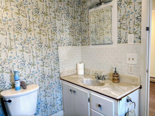 half bath with toilet, wallpapered walls, vanity, and a baseboard radiator