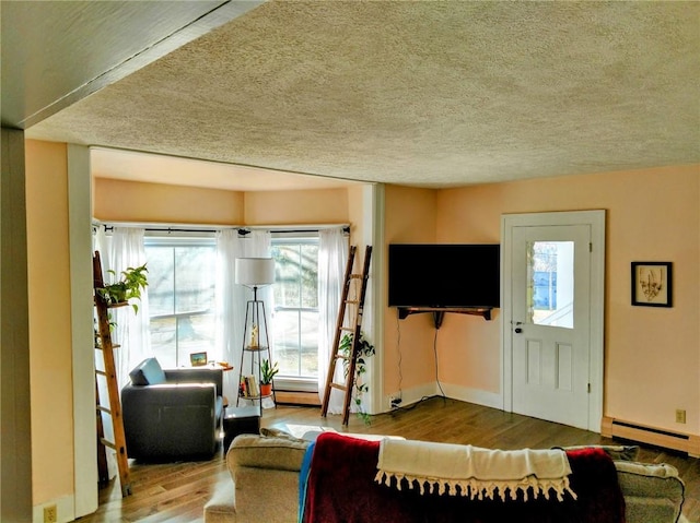 living room with wood finished floors, baseboards, baseboard heating, and a textured ceiling