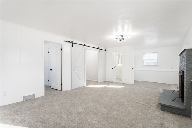 unfurnished living room featuring visible vents, carpet flooring, a fireplace, and a barn door