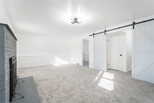 unfurnished living room featuring a fireplace, a barn door, and carpet