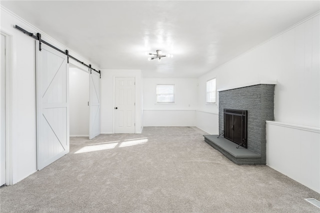 unfurnished living room with a barn door, carpet floors, and a brick fireplace