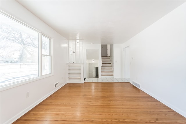 unfurnished living room with stairway, baseboards, visible vents, and light wood-style flooring