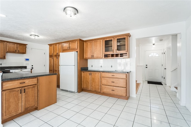 kitchen with brown cabinets, tasteful backsplash, freestanding refrigerator, light tile patterned floors, and glass insert cabinets