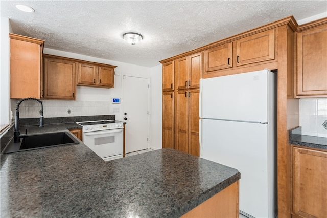 kitchen featuring brown cabinets, a sink, dark countertops, white appliances, and decorative backsplash