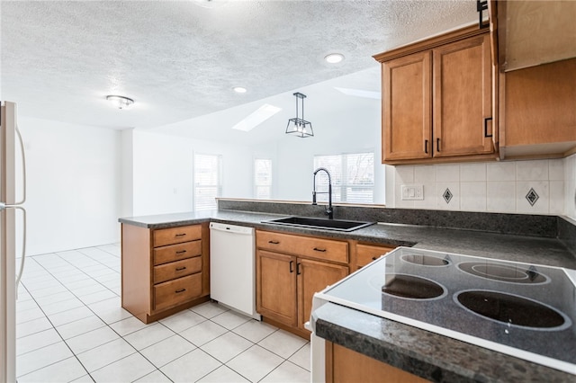 kitchen featuring dark countertops, a peninsula, brown cabinetry, white appliances, and a sink