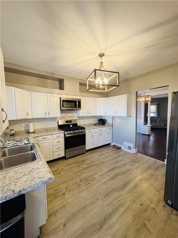 kitchen featuring light wood finished floors, white cabinetry, stainless steel appliances, and a sink