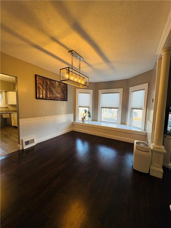 unfurnished room with visible vents, a textured ceiling, wood finished floors, wainscoting, and decorative columns