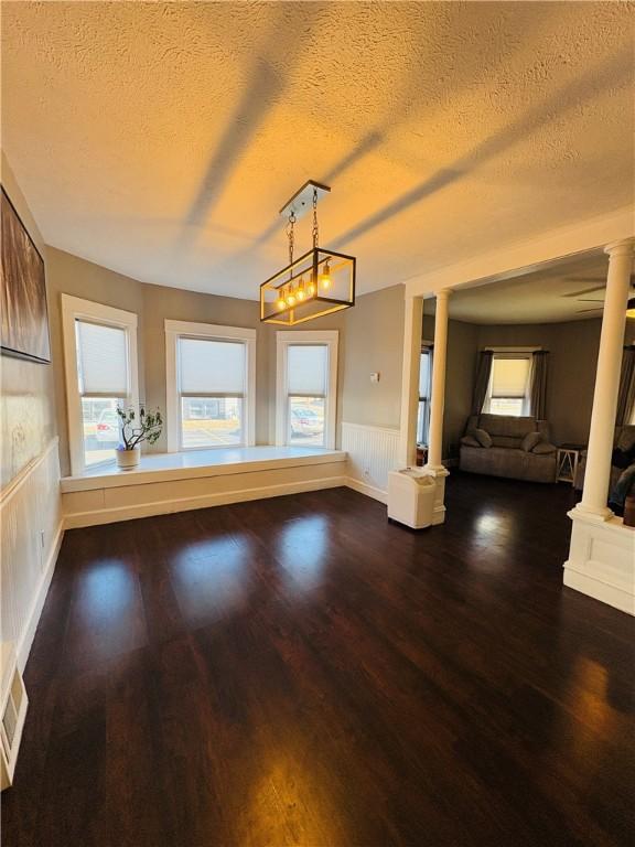 interior space with wood finished floors, visible vents, a wainscoted wall, decorative columns, and a textured ceiling