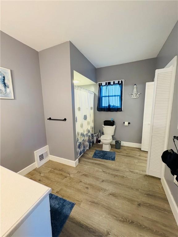 full bath with a shower with curtain, wood finished floors, visible vents, baseboards, and toilet