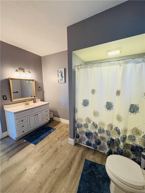 bathroom featuring toilet, wood finished floors, a shower with shower curtain, baseboards, and vanity