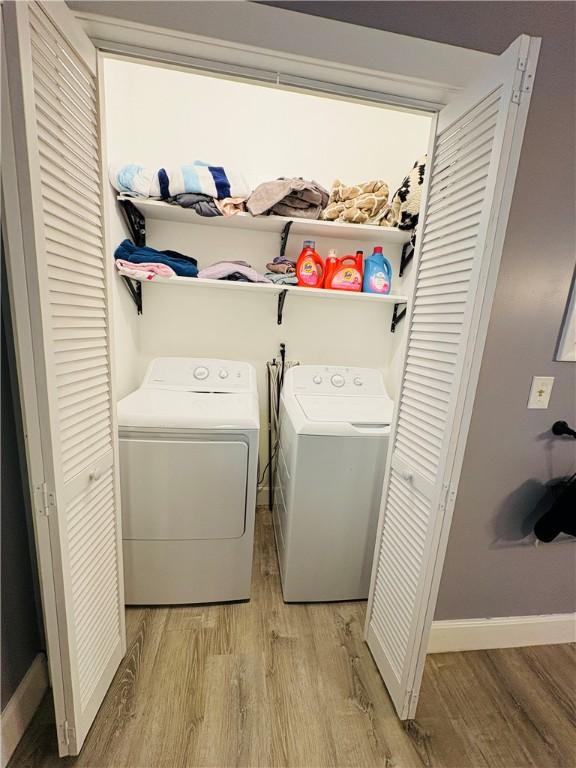 clothes washing area with laundry area, baseboards, light wood-type flooring, and washer and clothes dryer