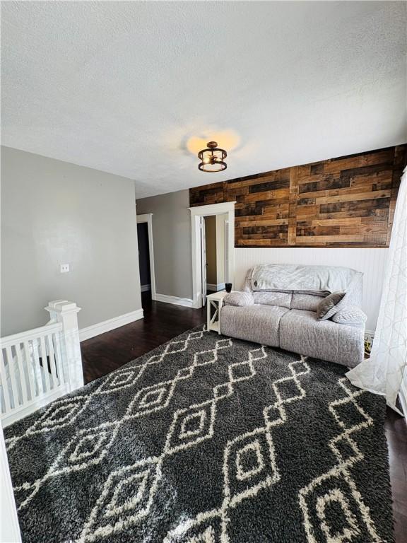 living room with wooden walls, wood finished floors, baseboards, and a textured ceiling