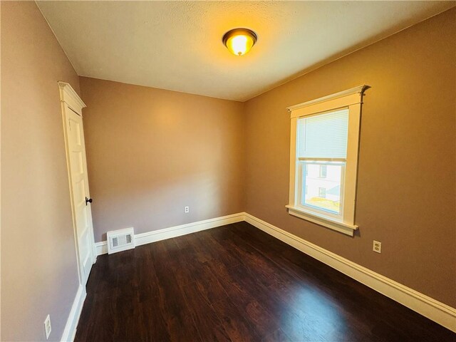 spare room featuring visible vents, baseboards, and dark wood-style flooring