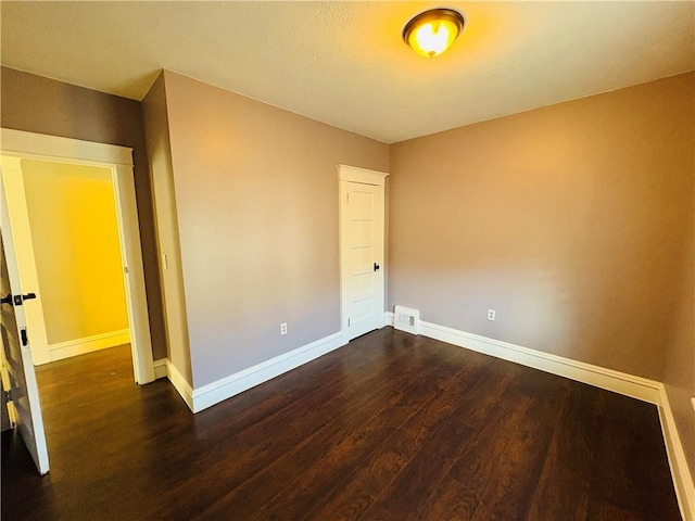 empty room with dark wood-type flooring, baseboards, and visible vents