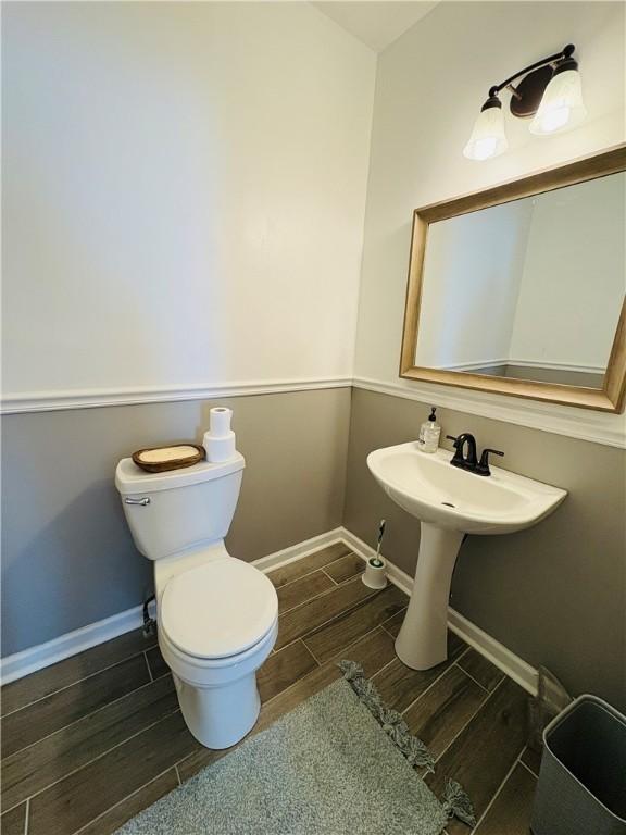 half bath with baseboards, toilet, and wood finish floors