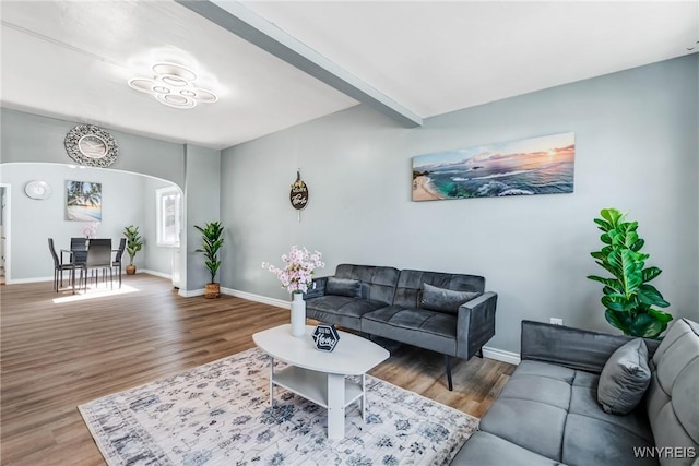 living room featuring beam ceiling, wood finished floors, arched walkways, and baseboards