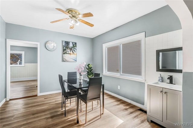 dining area featuring a ceiling fan, baseboards, light wood finished floors, and arched walkways