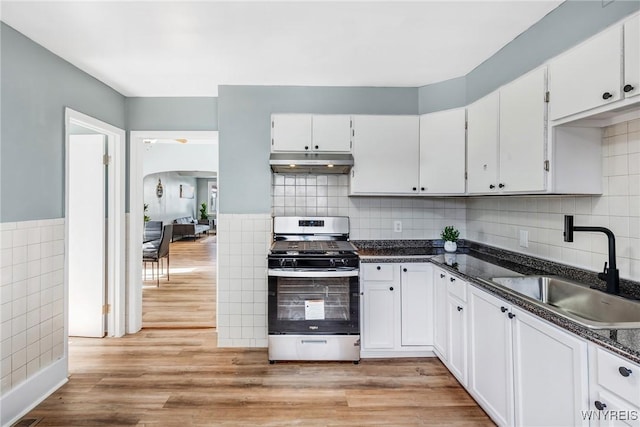 kitchen featuring under cabinet range hood, a sink, dark countertops, gas stove, and arched walkways