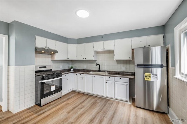 kitchen with dark countertops, under cabinet range hood, light wood-style floors, stainless steel appliances, and a sink