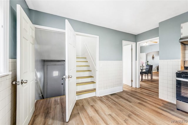 foyer with stairway, arched walkways, light wood-style floors, tile walls, and wainscoting