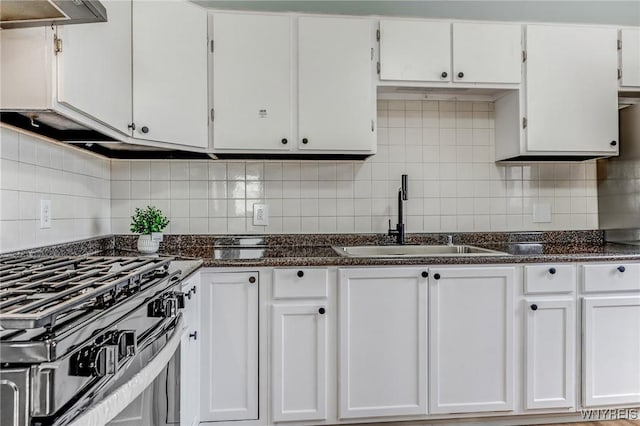 kitchen featuring backsplash, ventilation hood, gas range oven, white cabinets, and a sink