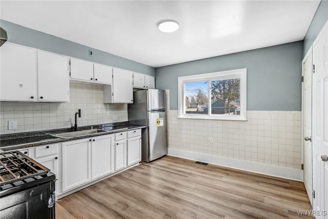 kitchen with visible vents, light wood finished floors, freestanding refrigerator, a sink, and white cabinetry