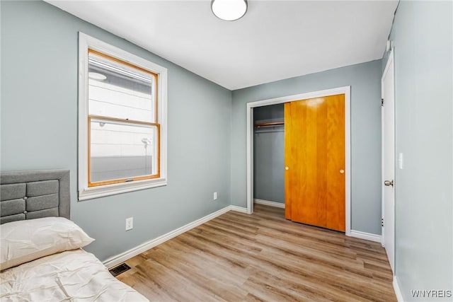 unfurnished bedroom with visible vents, wood finished floors, baseboards, and a closet