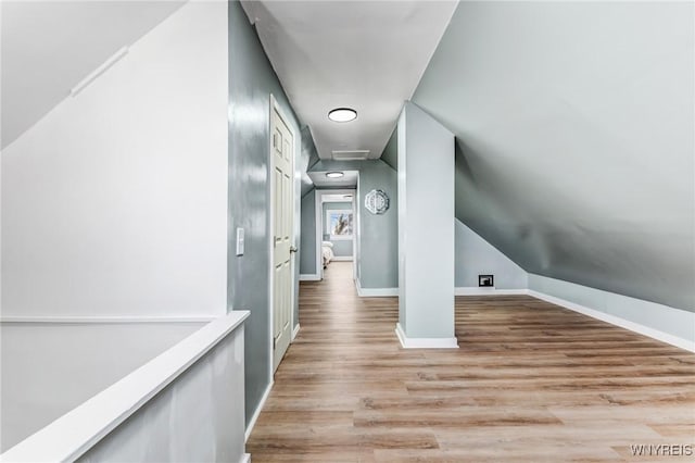 hall with light wood-type flooring, baseboards, lofted ceiling, and attic access