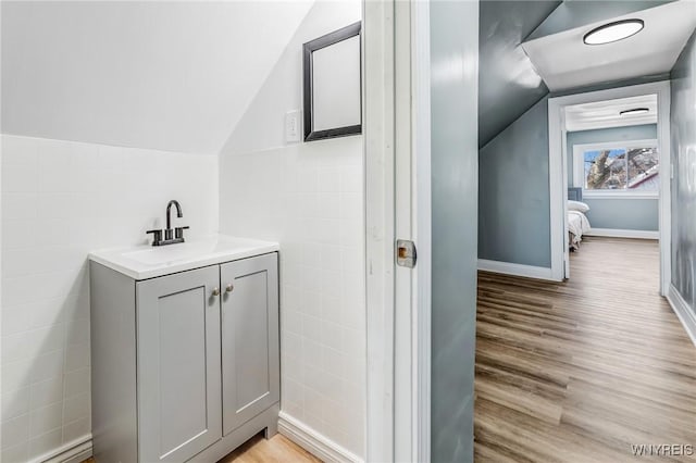 bathroom with lofted ceiling, tile walls, wood finished floors, and vanity