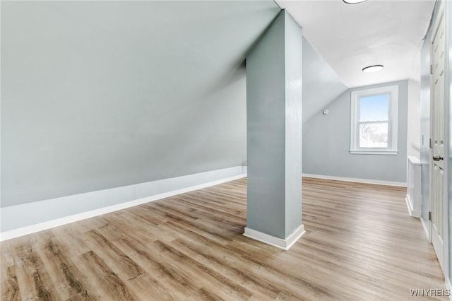 additional living space featuring baseboards, light wood-style flooring, and vaulted ceiling