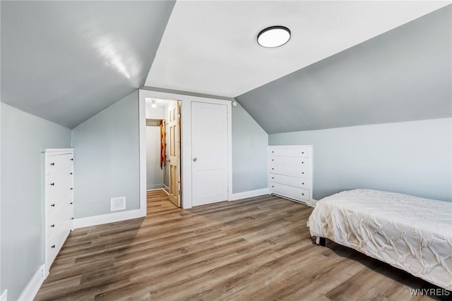 bedroom with lofted ceiling, wood finished floors, visible vents, and baseboards