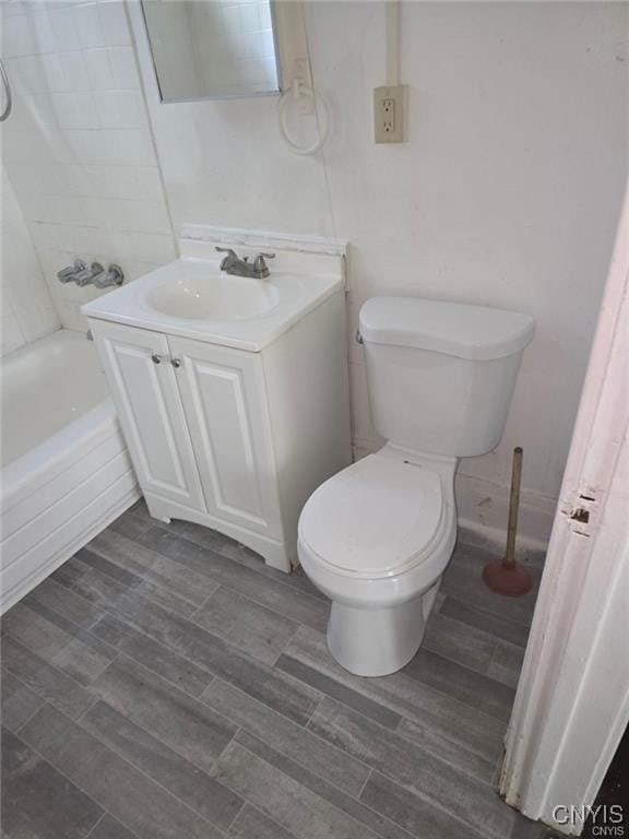 bathroom featuring wood tiled floor, washtub / shower combination, toilet, and vanity