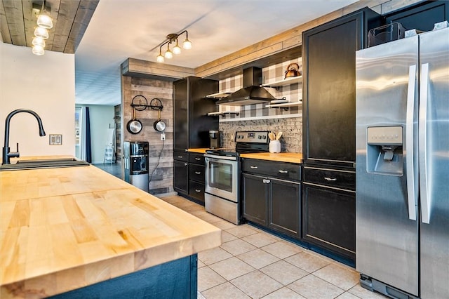 kitchen with open shelves, a sink, appliances with stainless steel finishes, wall chimney exhaust hood, and butcher block counters