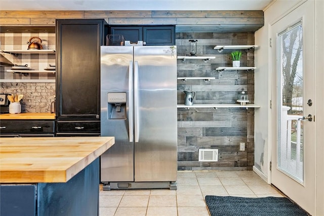 kitchen featuring visible vents, butcher block countertops, light tile patterned floors, stainless steel refrigerator with ice dispenser, and open shelves