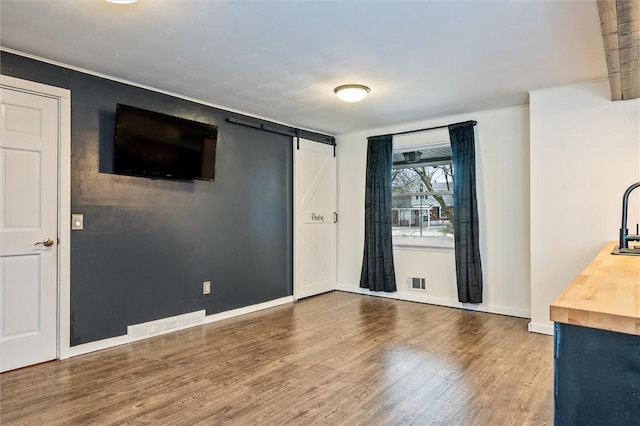 interior space with visible vents, baseboards, a barn door, and wood finished floors