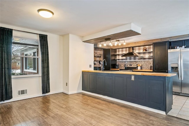 bar featuring visible vents, a sink, stainless steel appliances, light wood-style floors, and wall chimney range hood