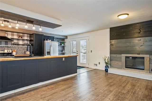 kitchen with a sink, wooden counters, appliances with stainless steel finishes, wall chimney exhaust hood, and open shelves