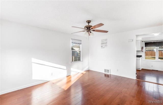 unfurnished living room featuring visible vents, baseboards, dark wood-type flooring, and ceiling fan