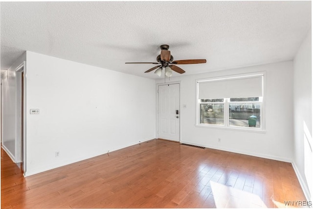 spare room with visible vents, baseboards, ceiling fan, wood finished floors, and a textured ceiling