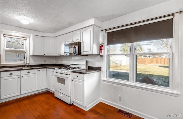 kitchen featuring dark countertops, visible vents, black microwave, white range with gas stovetop, and a sink