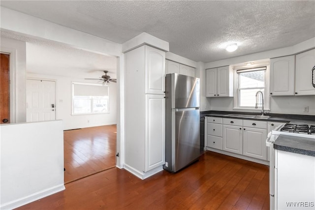 kitchen with dark wood-style floors, white range with gas cooktop, freestanding refrigerator, a sink, and dark countertops