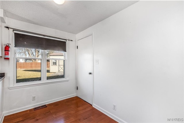 unfurnished room with baseboards, wood finished floors, visible vents, and a textured ceiling