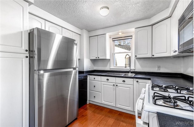 kitchen featuring dark wood-style floors, a sink, black appliances, white cabinetry, and dark countertops