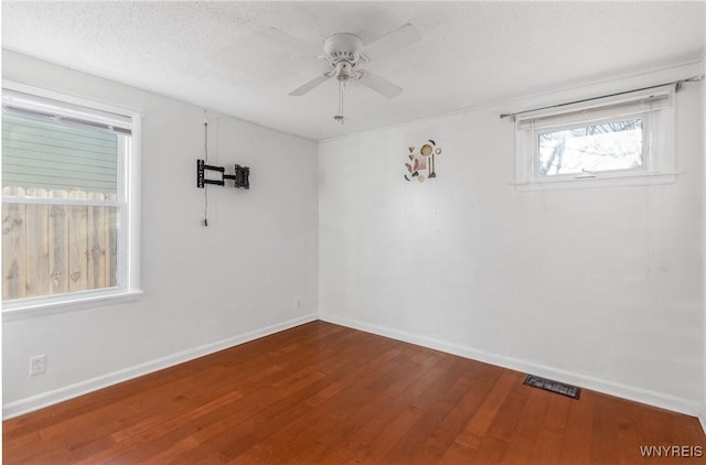 spare room with visible vents, a ceiling fan, a textured ceiling, wood finished floors, and baseboards